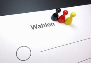Bild vergr&ouml;&szlig;ern: Drei Spielfiguren stehen in der Farbe der deutschen Flagge auf einem Wahlzettel.